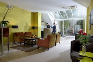 Un moderno vestíbulo de hotel con una pared amarilla, un mostrador de recepción, zona de estar y un amplio ventanal con vistas al exterior.