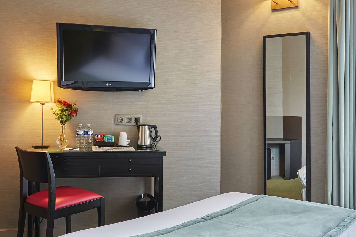 Habitación de hotel con cama, escritorio, silla, televisor de pantalla plana, espejo y lámpara.