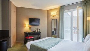 A hotel room with a bed, a desk with a chair, a television, and a window with curtains. - Hôtel Orchidée (Paris)