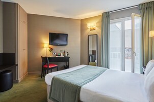 Una habitación de hotel con cama, escritorio con silla, televisor y ventana con cortinas.