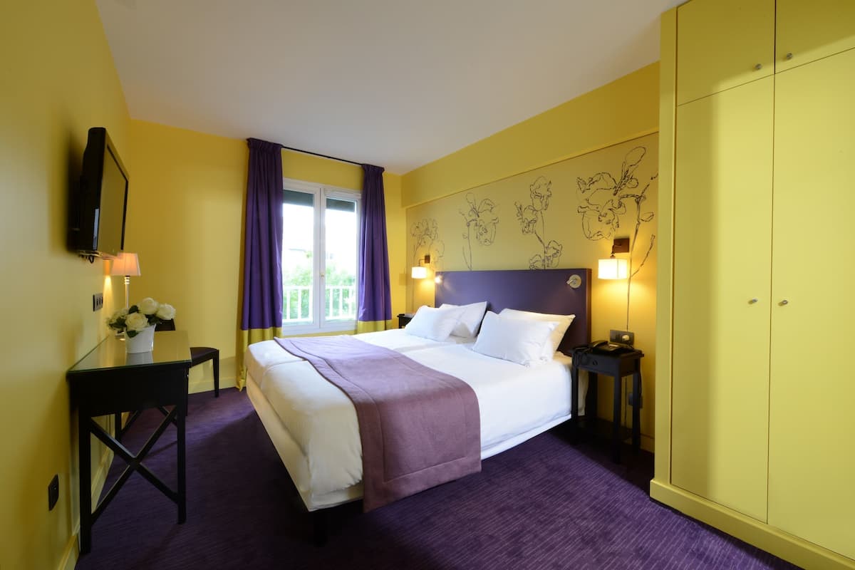 Una habitación de hotel con cama, escritorio, armario y ventana con cortinas.