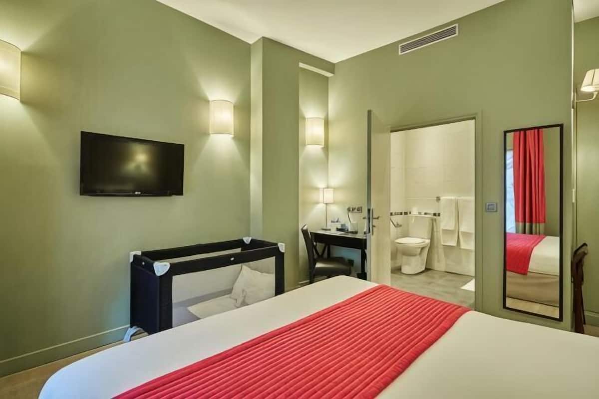 Habitación de hotel con cama, escritorio, silla, televisor, espejo y baño.