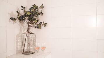 A clear glass vase with a plant on a white tiled surface.