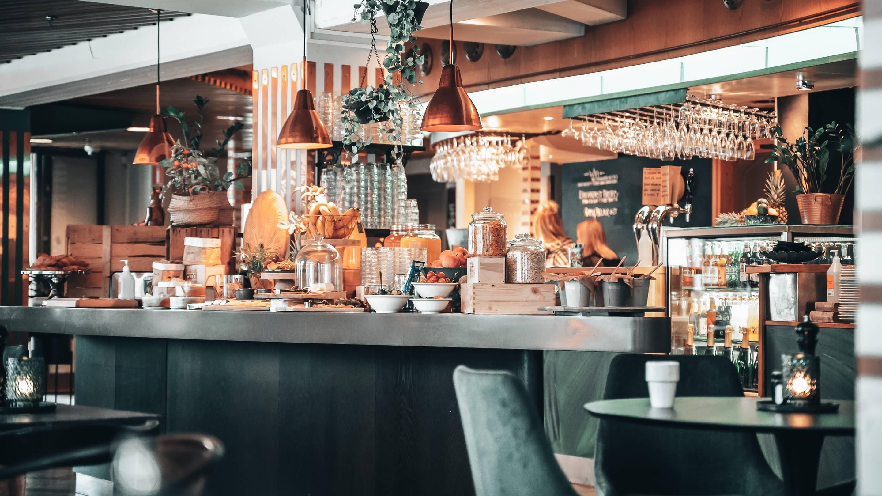 En modern bardel med ett varierat utbud av mat och dryck, inklusive ett bord med färska frukter och en kaffestation.