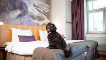 A hotel room with a bed, a headboard, a window with curtains, and a painting on the wall.