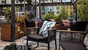 Un área de estar al aire libre con muebles de mimbre, plantas en macetas y luces colgantes.