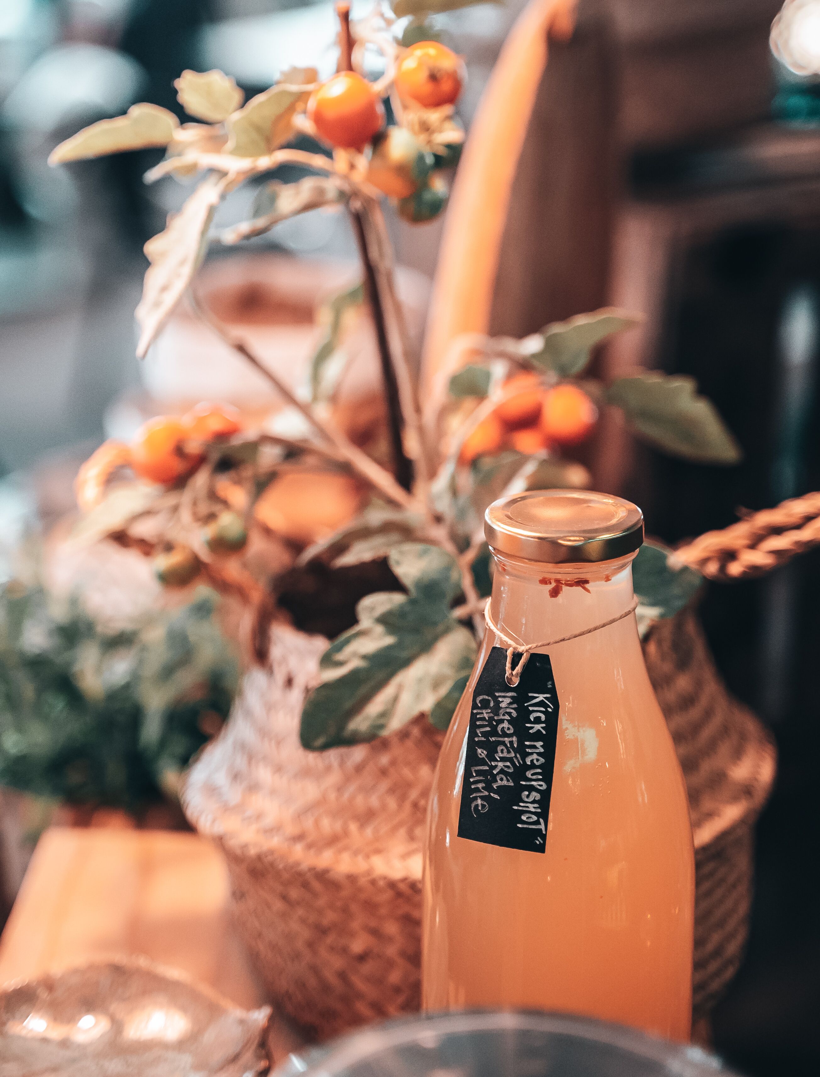 Una botella de vidrio con etiqueta, una cesta de mimbre con hojas verdes y frutas naranjas, y un fondo desenfocado.