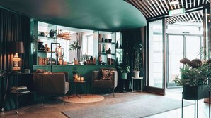 Una sala de estar acogedora con una pared verde de acento, un sofá cómodo, una mesita de centro pequeña y varios objetos decorativos y plantas.