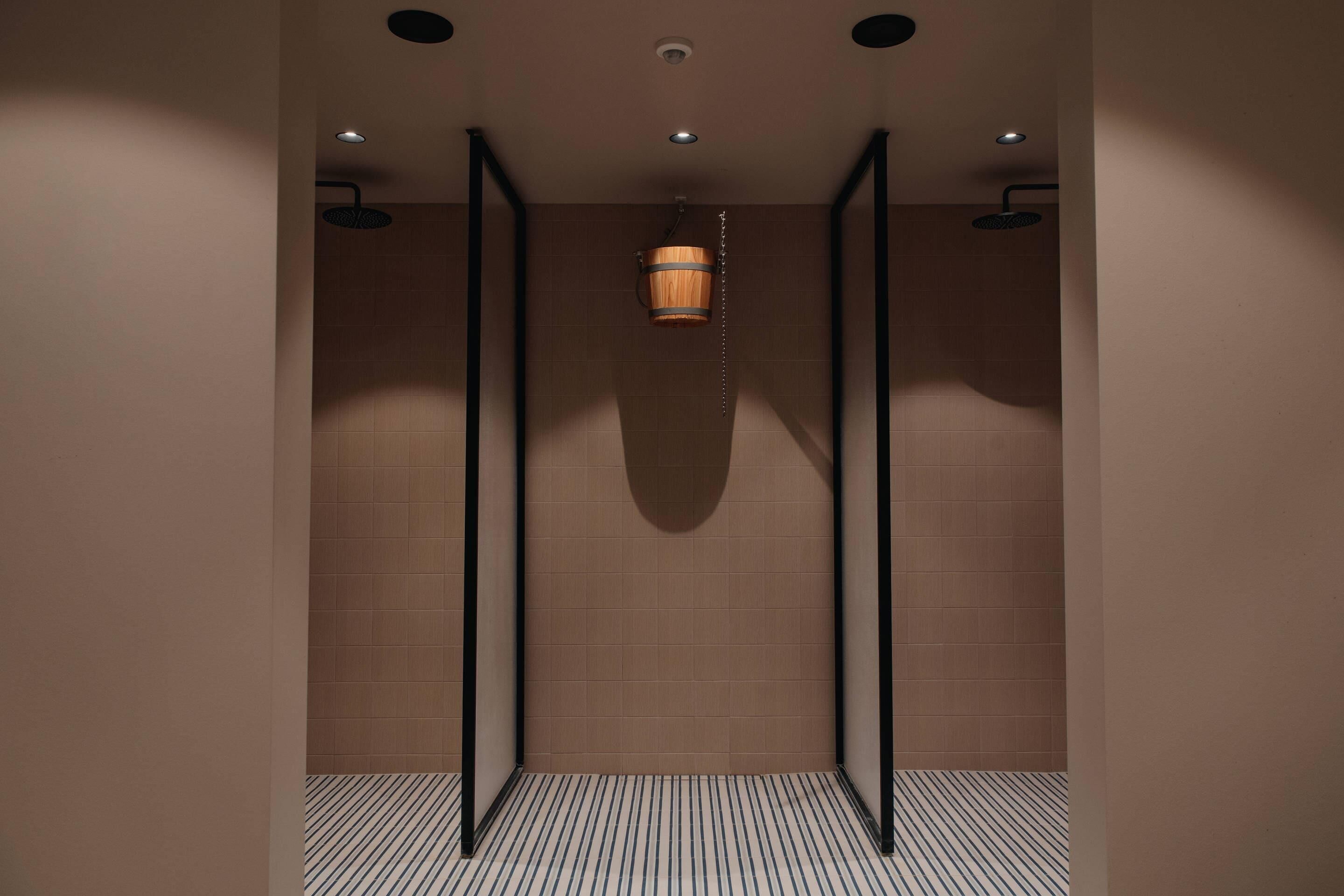 A modern bathroom with a wooden bucket showerhead, black-framed glass doors, and a striped floor.