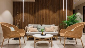 Una sala de estar moderna con un sofá, dos sillones de mimbre, una mesa de centro redonda y un panel de pared de madera vertical.