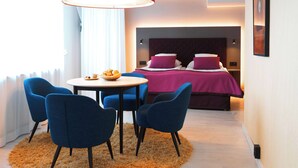 Een moderne hotelkamer met een bed, een rond tafel met stoelen, een rode lamp en een ingelijst kunstwerk aan de muur.