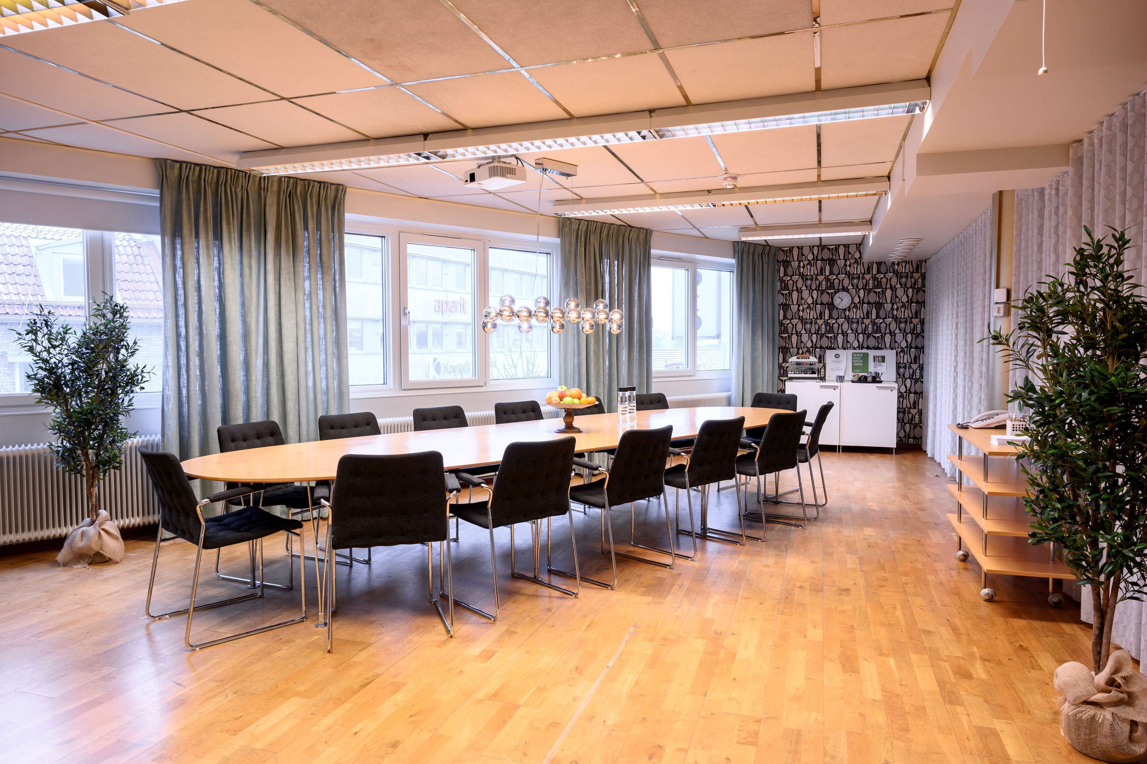 Een vergaderruimte met een lange tafel, zwarte stoelen en een kroonluchter.