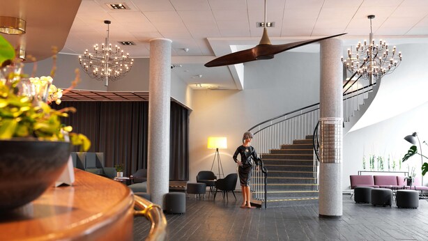 Een moderne lobby met een centrale trap, een grote kroonluchter en een kamerplant.