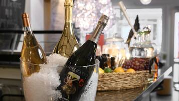 A bar area with bottles of champagne in a glass bowl on ice, a basket of fruits, and a wine bottle on the counter.