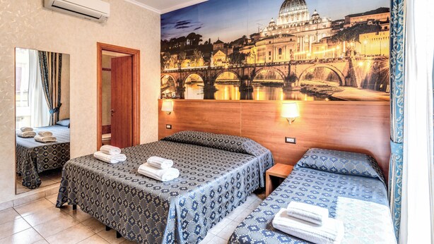 Une chambre d’hôtel avec deux lits, une grande fresque représentant un paysage urbain, une porte en bois et un miroir.