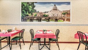 Un espace repas avec des tables préparées pour deux personnes, agrémenté d’une grande fresque murale représentant un paysage urbain.