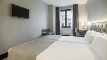 A hotel room with a bed, a desk, a chair, a TV, and a window with curtains.