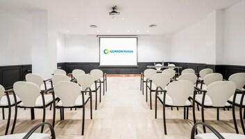 A conference room with a projector screen displaying the ILUNION Hotels logo, arranged seating, and a table with chairs.