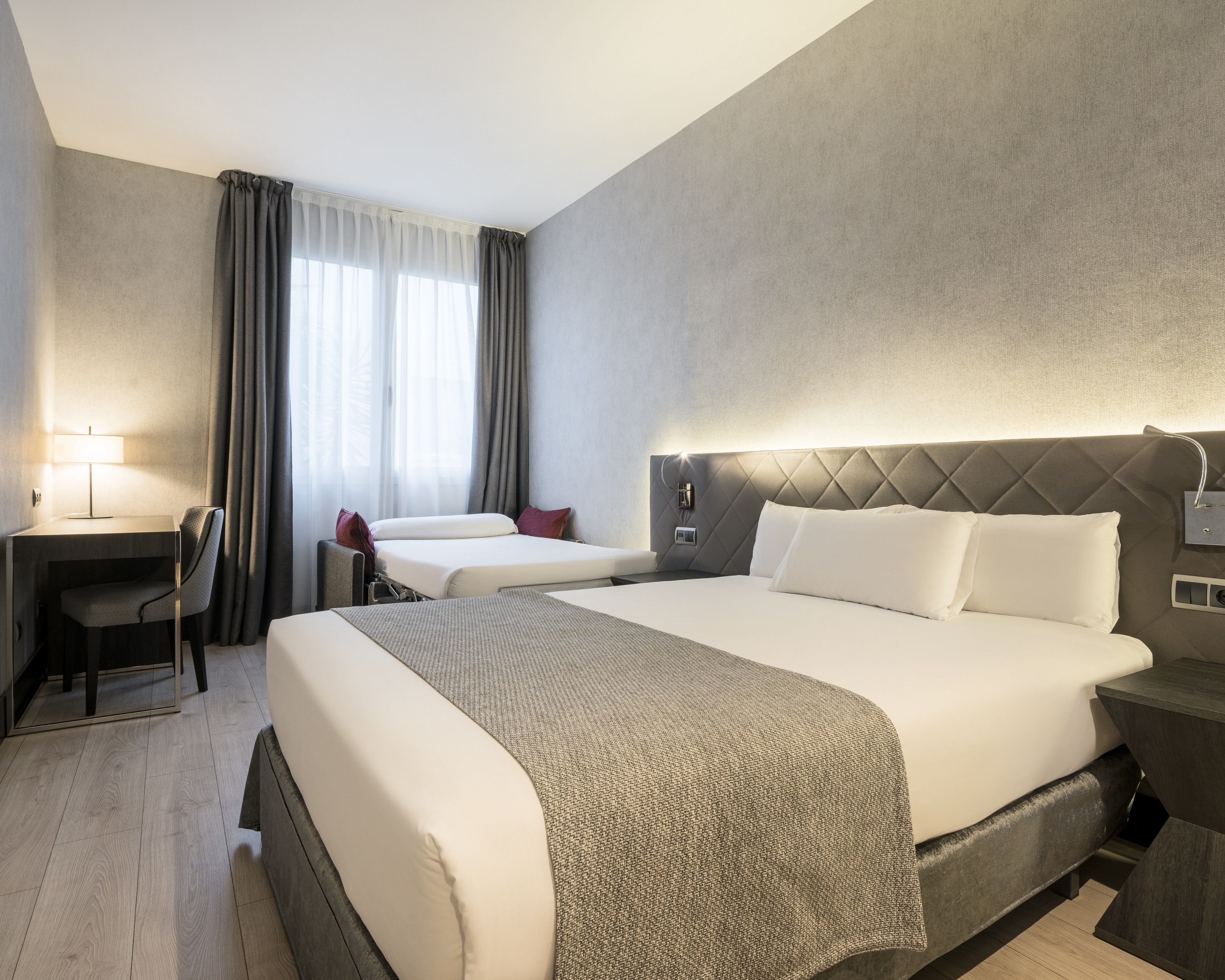 A hotel room with a large bed, a desk, and a chair.