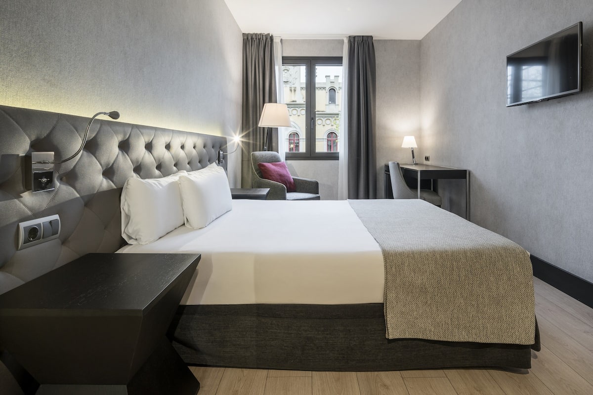 Et moderne hotelværelse med en stor seng, et fladskærms-TV, et skrivebord og en stol.