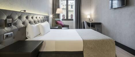 A modern hotel room with a large bed, a flat-screen TV, a desk, and a chair.