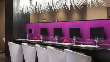 A modern bar area with white chairs, a purple counter, and hanging light fixtures.