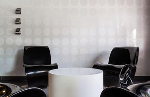 Um banheiro moderno com um espelho circular, duas cadeiras pretas e parede estampada.