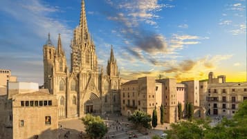 Una catedral histórica con un gran campanario central y múltiples torres, rodeada por un patio con árboles y algunas personas.