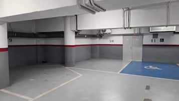 Un parking souterrain avec des places de stationnement numérotées, une place de stationnement bleue réservée aux personnes handicapées et des conduits de ventilation au plafond.