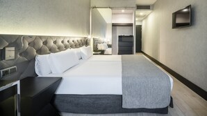 Una habitación de hotel moderna con una cama grande, una mesita de noche, un televisor y un baño visible a través de una puerta abierta.
