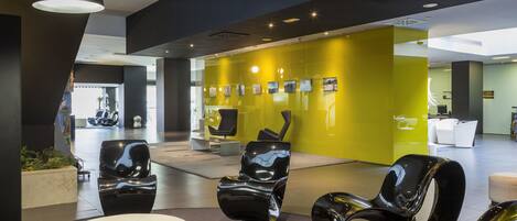 A modern lobby with black and white chairs, a yellow accent wall, and a reception area.