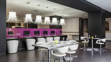 Uma área de refeições moderna com uma mesa comprida, cadeiras brancas e luminárias pendentes.