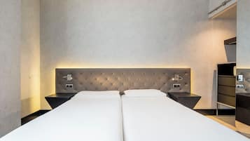 Una cama doble con cabecera capitonada, dos mesitas de noche y una mesita auxiliar con lámpara.