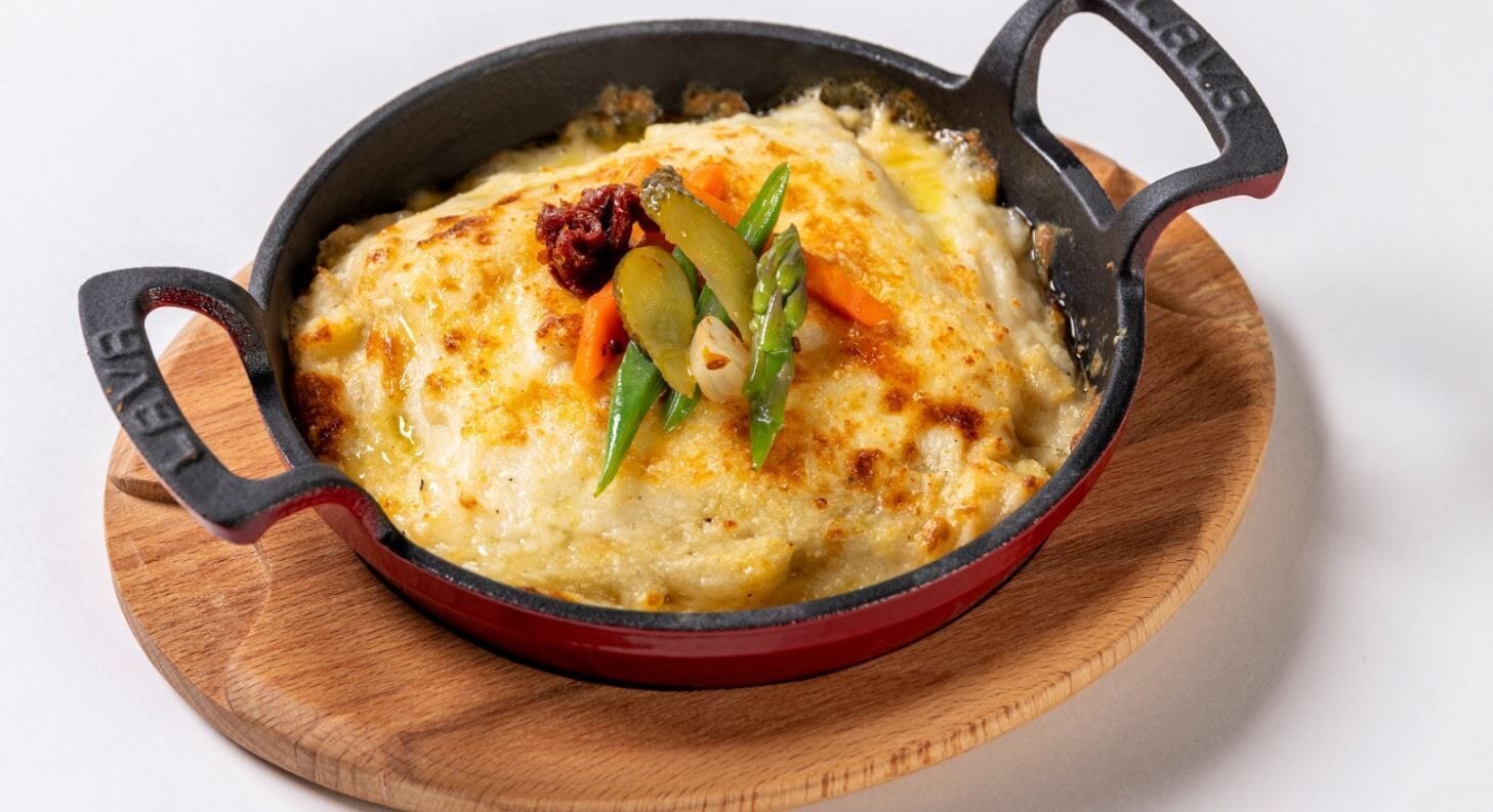 A cast iron skillet with a baked dish, possibly a casserole, on a wooden board.