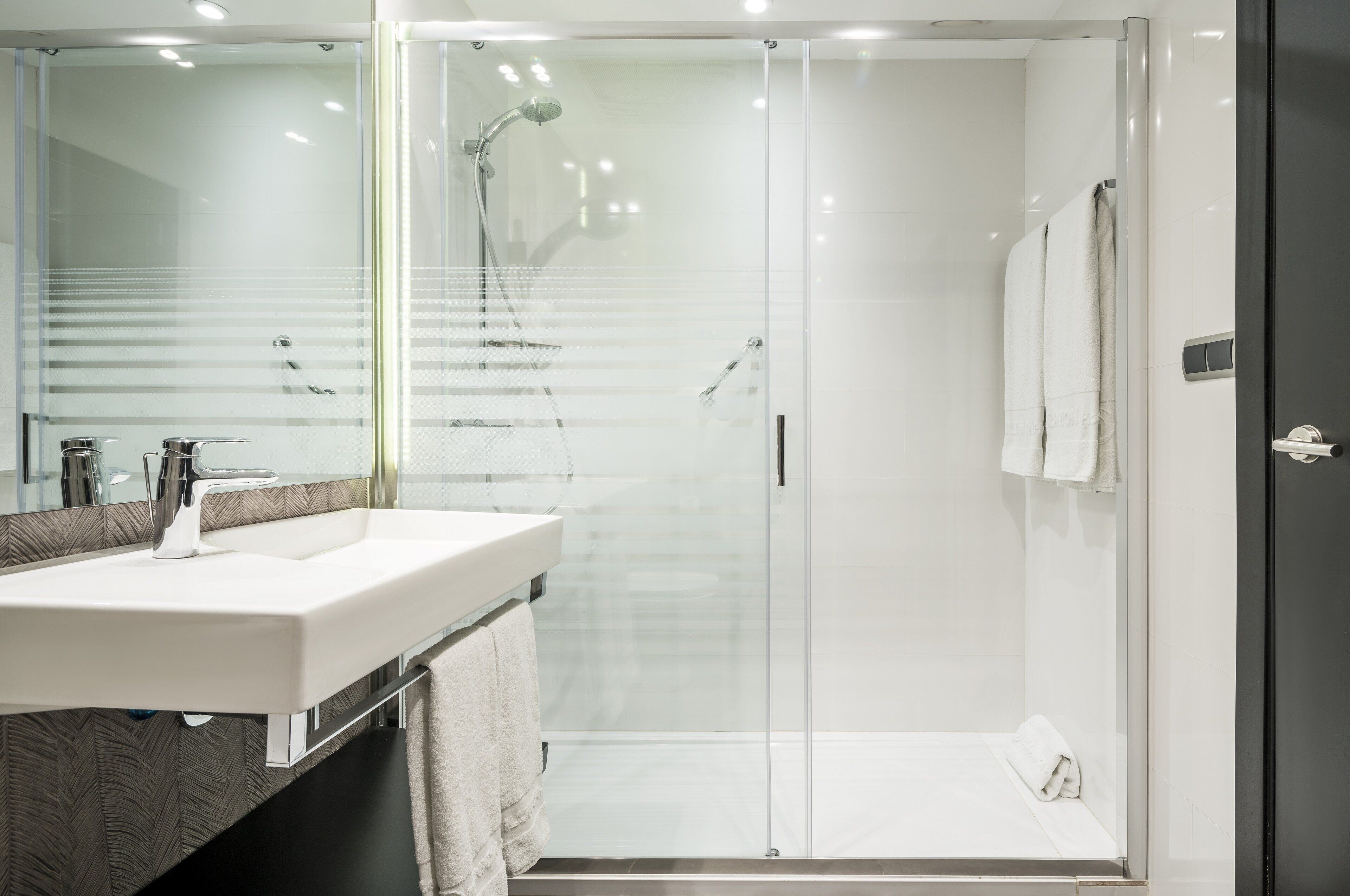 Un baño moderno con ducha de vidrio, lavamanos blanco y espejo.