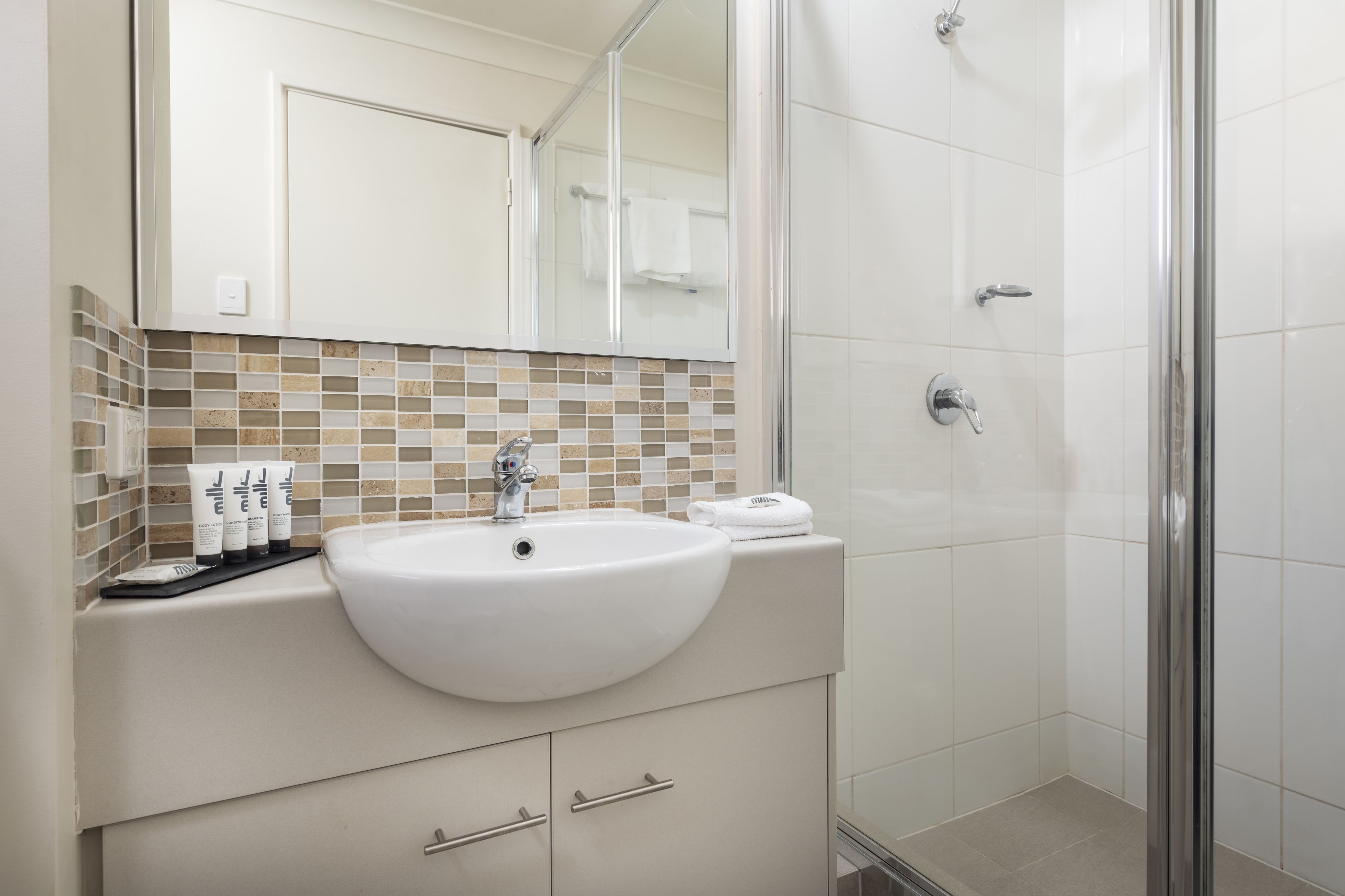 A bathroom with a white sink, a mirror, a shower, and a tiled backsplash.