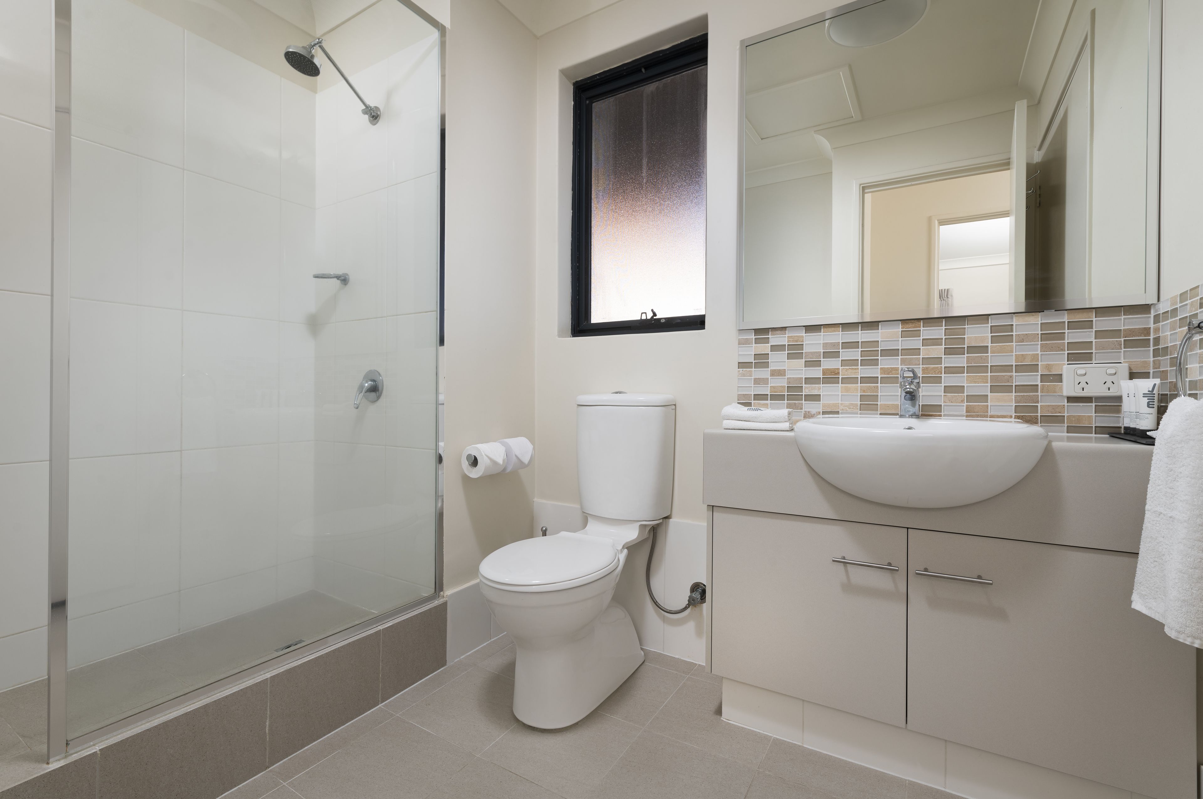 A modern bathroom with a glass shower enclosure, a toilet, and a sink with a tiled backsplash.
