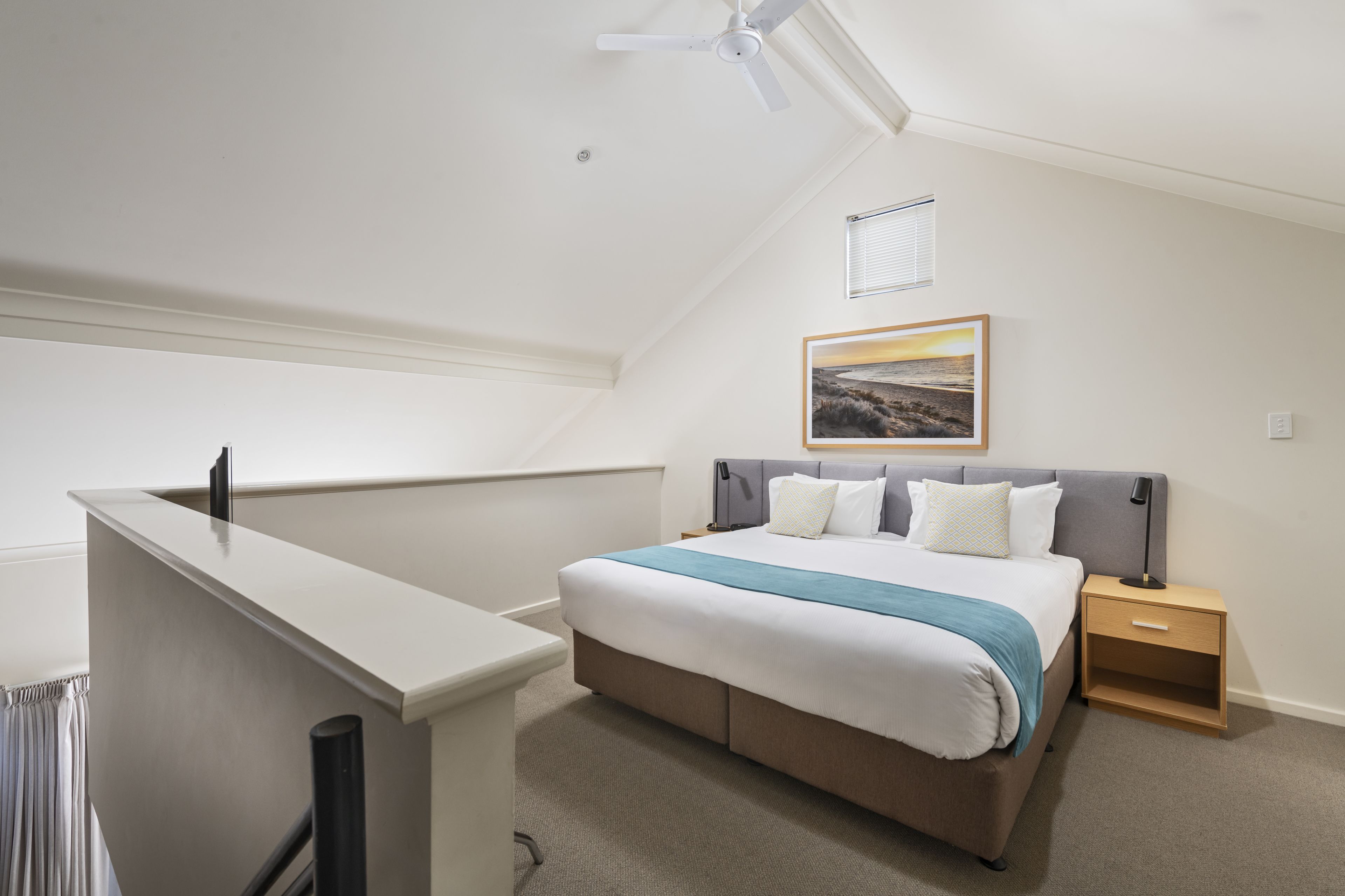 Un dormitorio con cama, mesitas de noche, ventilador de techo y ventana con persianas.