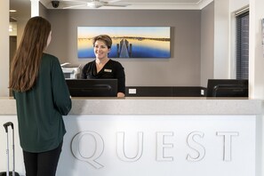 Ein Empfangstresen mit einer Namensschild, auf der 'QUEST' steht, und einem Gemälde eines Piers an der Wand.