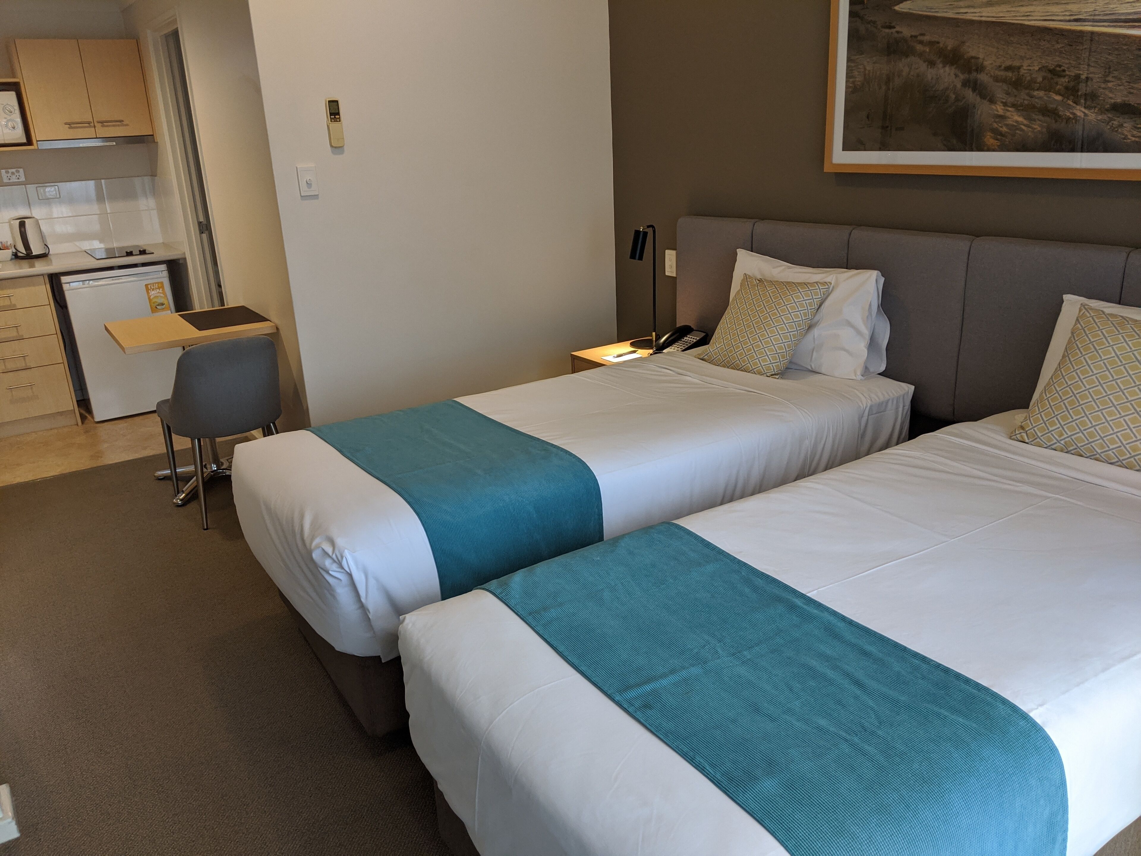 Habitación de hotel con dos camas, un escritorio y una kitchenette.