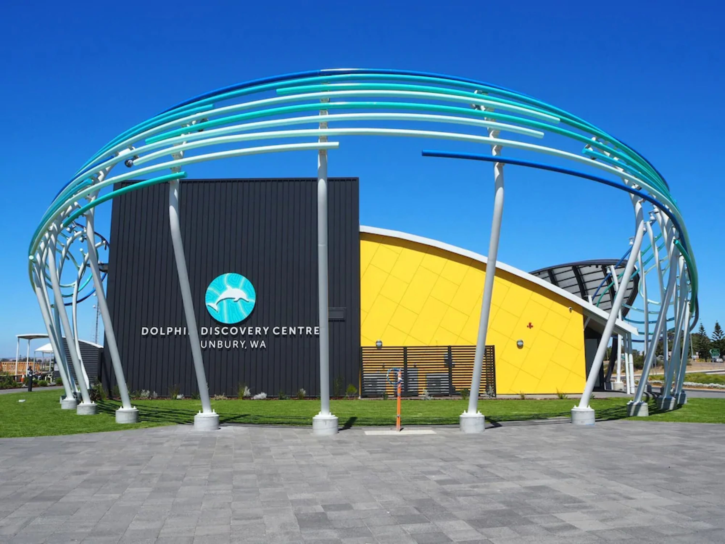 The Dolphin Discovery Centre in Unbury, WA, featuring a modern design with a yellow facade and a distinctive blue and white arch structure.