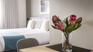 Une chambre d’hôtel avec un lit, une table ornée d’un vase de fleurs et une fenêtre avec des rideaux.