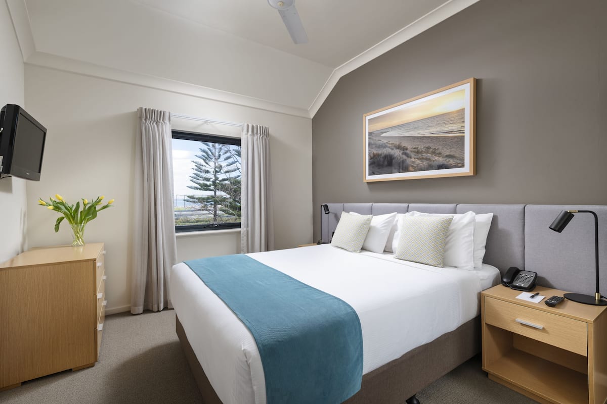 Une chambre d’hôtel avec un lit, une table de chevet, une lampe, un téléphone et un tableau au mur.