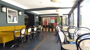 Un restaurante moderno con sofás amarillos, sillas negras y de mimbre, y piso de baldosas.