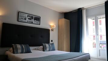 Ett hotellrum med en stor säng, en sänggavel, en tavla som hänger på väggen, en garderob och utsikt genom en glasdörr.