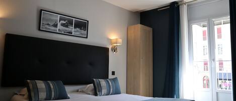 A hotel room with a large bed, a headboard, a wall-mounted picture, a wardrobe, and a view through a glass door.