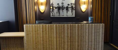 A reception desk with a patterned backdrop, a framed photograph above it, and two wall-mounted lamps.