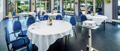 Un salón de conferencias con mesas redondas, sillas y un soporte para proyector.