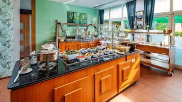 A buffet setup with a variety of food items, a coffee station, and a view of greenery outside.