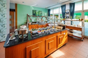 A buffet setup with a variety of food items, a coffee station, and a view of greenery outside. - Best Western Spreewald (Lübbenau/Spreewald)